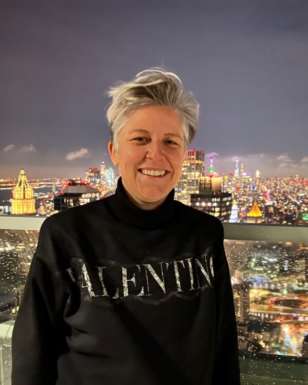 Lauren Proctor smiling on a rooftop at night, with the lit-up Manhattan skyline behind her.